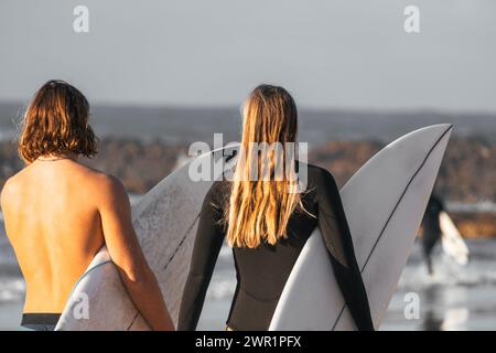 Ein paar Surferfreunde laufen zusammen am Strand und halten ihre Surfbretter Stockfoto