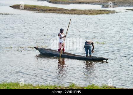 Zwei Dorfbewohner fischen von einem Kanu aus auf einer Lagune eines Flusses in Afrika; einer stößt das Boot und einer wirft das Fischernetz Stockfoto