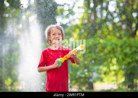 Kinder spielen mit einem Wasserschlauch. Sommergarten Outdoor Spaß für Kinder. Ein Junge spritzt Wasser an einem heißen, sonnigen Tag. Kinder, die Pflanzen im Garten bewässern. Stockfoto