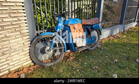 Vintage alt, restaurierungsbedürftig blaues Motorrad mit abgenutztem hellbraunen Ledersitz neben rustikaler handgefertigter Leder-Motorradtasche Stockfoto