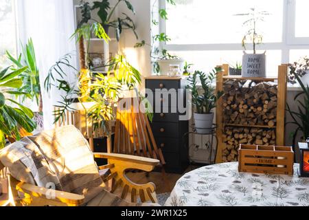 Tropische Zimmerpflanzen im Innenraum weißes Loft im Landhaus, Holzmöbel, Brennholz für Kamin im Sonnenlicht. Zimmerpflanzenanbau und Stockfoto