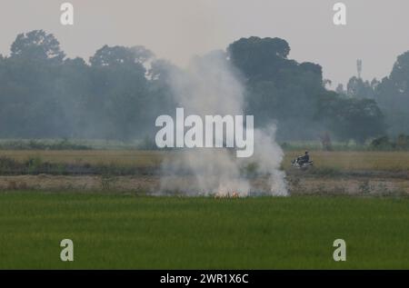 Bangkok, Thailand. März 2024. Ein Dorfbewohner fährt mit dem Motorrad vorbei an einem brennenden Reisfeld in der Provinz Nakhon Sawan, nördlich von Bangkok. (Credit Image: © Chaiwat Subprasom/SOPA Images via ZUMA Press Wire) NUR REDAKTIONELLE VERWENDUNG! Nicht für kommerzielle ZWECKE! Stockfoto