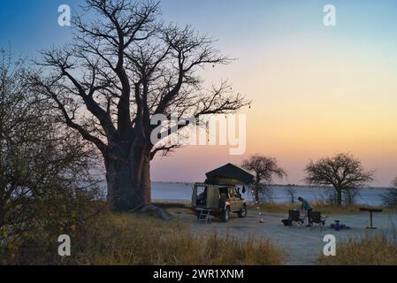 Ein wilder Campingplatz neben einem Baobab-Baum auf einer Insel, umgeben von einem trockenen Salzsee. Das Zelt auf dem Dach des Geländefahrzeugs ist einsatzbereit. Stockfoto