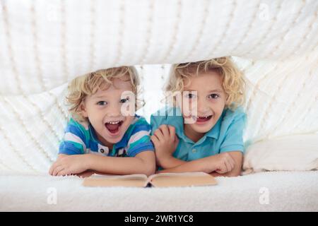 Lesebuch für Kinder im Bett unter der Strickdecke. Zwei Brüder spielen zusammen. Kinder gemütliches Zimmer im Hyggge-Stil. Kleiner Junge, der Hausaufgaben macht, bevor er schläft. Stockfoto