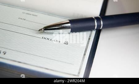 Ein blauer Stift befindet sich auf einem leeren Scheck, dessen Spitze in der Nähe der Zeile für den Zahlungsbetrag liegt, sodass jemand die erforderlichen Details ausfüllen kann Stockfoto