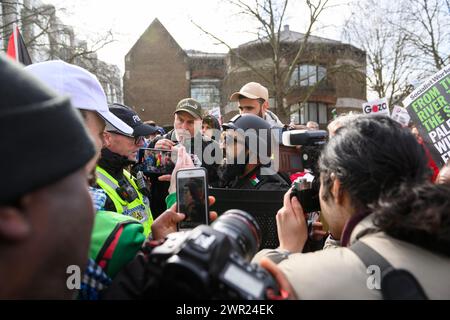 Ein Demonstrant, der einen Helm im Militärstil trägt und einen Aufruhrschild auf einem Pro-Palästina-marsch trägt, wird von der Polizei befragt. Der marsch ist kal Stockfoto