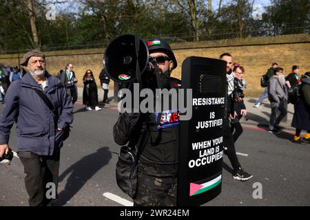 Ein Demonstrant, der einen Helm im Militärstil trägt und einen Aufruhrschild auf einem Pro-Palästina-marsch trägt, der zu einem Waffenstillstand des laufenden Militärs von aufruft Stockfoto