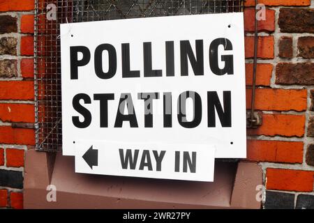 Ein großes schwarz-weißes Schild an der Außenfassade des Gebäudes, auf dem die Polling Station steht, mit einem Pfeil, der den Weg hineinweist Stockfoto