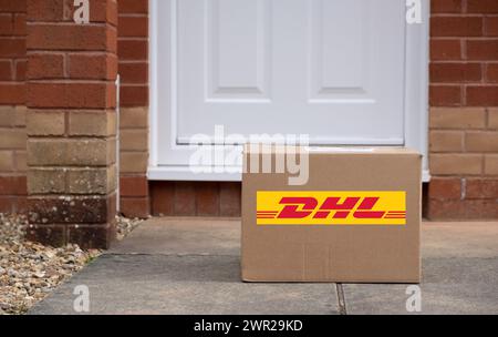 Exeter, UK-10. März 2024: Ein DHL-Versandkarton vor einer Haustür. DHL ist ein deutsches Logistikunternehmen, das Kurier, Paketzustellung und Post anbietet Stockfoto