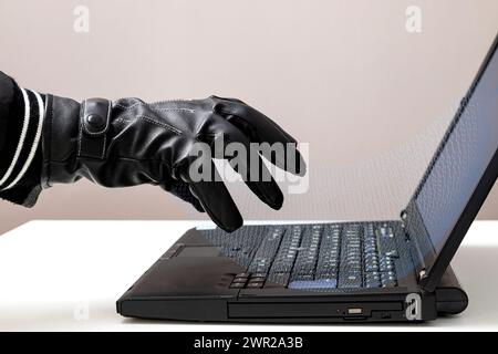 Eine Hand einer unbekannten Person, die einen schwarzen Lederhandschuh trägt, der Binärcode von einem Laptop-Bildschirm absorbiert. Stockfoto