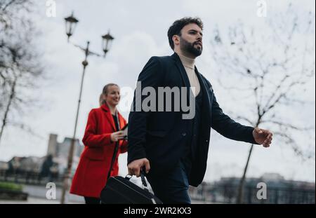 Selbstbewusster Geschäftsmann, der schnell mit einer Frau im roten Mantel im Hintergrund läuft Stockfoto