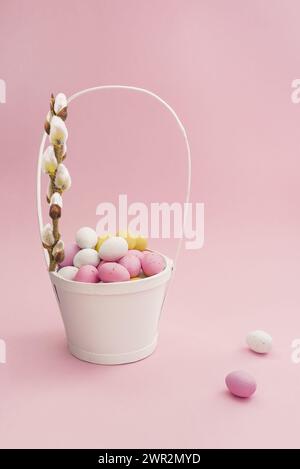 Weißer Osterkorb mit Schokoladeneiern und Weidenzweig auf pastellrosa Hintergrund. Osterkomposition. Karte mit Kopierraum für Text Stockfoto