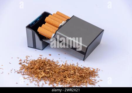 Eine Plastikkiste neben einem Stapel verstreuten Tabaks auf weißem Hintergrund. Stockfoto
