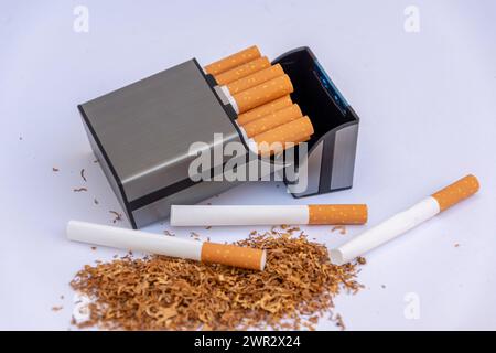 Zigarettenetui neben verstreutem Rauchtabak und leeren Zigarettenhüllen auf weißem Hintergrund. Stockfoto