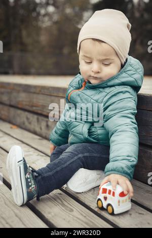 Kleiner Junge im Herbstpark posiert für Porträt auf Holzbank Stockfoto