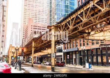 Der Zug fährt auf erhöhten Gleisen über eine Straße, die sowohl von modernen Hochhäusern als auch von traditionellen Backsteinhäusern im Zentrum von Chicago gesäumt ist Stockfoto