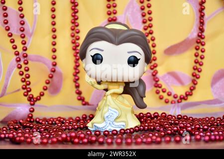 Funko Pop Actionfigur der Disney-Prinzessin Belle im gelben Kleid aus dem Animationsfilm Beauty and the Beast. Goldener rosa Vorhang, rote Halskette, fabelhaft. Stockfoto