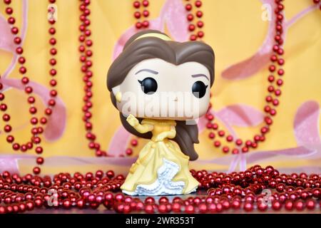 Funko Pop Actionfigur der Disney-Prinzessin Belle im gelben Kleid aus dem Animationsfilm Beauty and the Beast. Goldener rosa Vorhang, rote Halskette, fabelhaft. Stockfoto