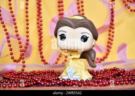 Funko Pop Actionfigur der Disney-Prinzessin Belle im gelben Kleid aus dem Animationsfilm Beauty and the Beast. Goldener rosa Vorhang, rote Halskette, fabelhaft. Stockfoto