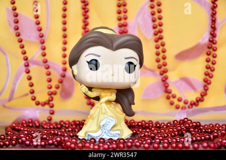 Funko Pop Actionfigur der Disney-Prinzessin Belle im gelben Kleid aus dem Animationsfilm Beauty and the Beast. Goldener rosa Vorhang, rote Halskette, fabelhaft. Stockfoto