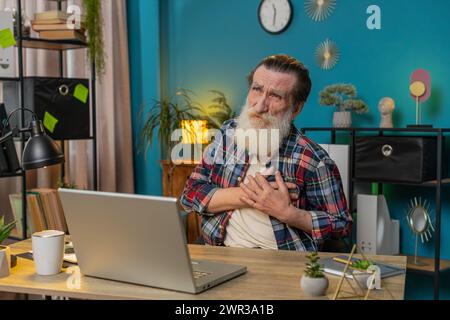 Kaukasischer gestresster Senior man Freelancer leidet unter Spannung, die Brust hält mit Herzschmerz Attack Risiko eines Schlaganfallsymptoms während der Arbeit an einem modernen Home Office Arbeitsplatz. Opa im karierten Hemd. Stockfoto