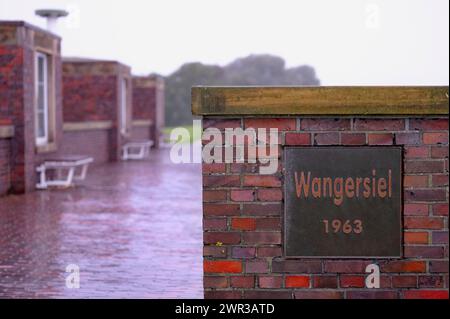 Wangersiel 193, Metallschild am Hafen von Horumersiel auf einer roten Backsteinmauer, in den Hintergrundbänken und dem asphaltierten Weg zum Deich Horumersiel Stockfoto