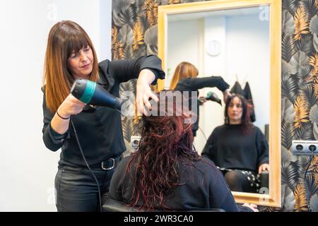 Friseurin, die das Haar einer Frau vor einem Spiegel im Salon trocknet Stockfoto