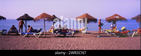 Sonnenanbeter mit Sonnenschirmen am Strand in Torre del Mar, Costa del Sol, Provinz Malaga, Andalusien, Spanien, Südeuropa. Gescannte Folie Stockfoto