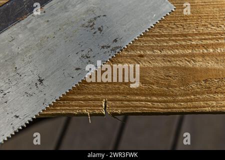 Gezackte Wirbelsäule einer handgehaltenen Holzbearbeitungssäge neben einem Stück Holz Stockfoto