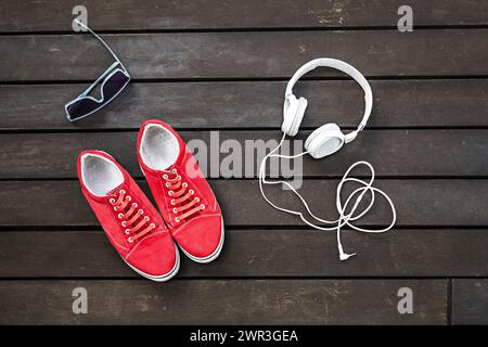 Rote Sneakers mit Kopfhörern und Sonnenbrille auf brauner Dielloberfläche Stockfoto