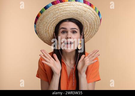 Überraschte junge Frau mit mexikanischem Sombrero-Hut auf beigefarbenem Hintergrund Stockfoto