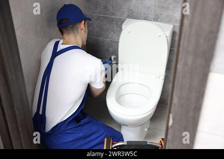 Klempner mit Schraubenschlüssel repariert Toilettenschüssel im Wasserschrank Stockfoto