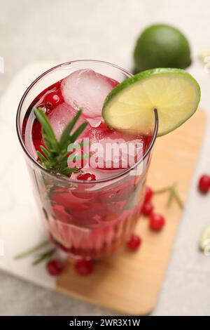 Leckerer Cranberry-Cocktail mit Rosmarin und Limette im Glas auf dem Tisch, Nahaufnahme Stockfoto