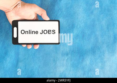 Online-Jobkonzept. Hand hält ein Mobiltelefon mit einem Wort auf blauem Hintergrund. Stockfoto