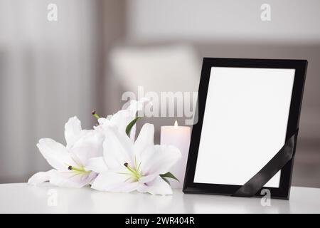 Fotorahmen mit schwarzem Band, weißen und violetten Lilien auf weißem Tisch drinnen. Leerzeichen für Text Stockfoto