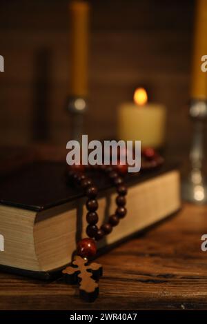 Kreuz, Bibel, Rosenkranzperlen und Kirchenkerzen auf Holztisch, Nahaufnahme Stockfoto