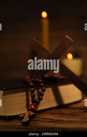 Bibel, Kreuz, Rosenkranzperlen und Kirchenkerzen auf Holztisch, Nahaufnahme Stockfoto