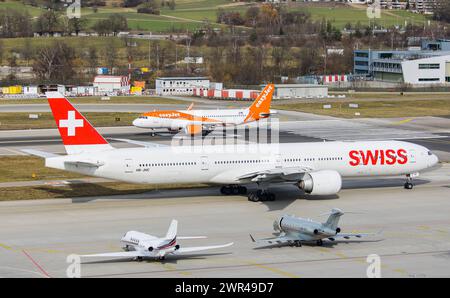 Auf der Startbahn 28 des Flughafen Zürich startete ein Airbus A320-214 von EasyJet. Dahhinter wartet eine Boeing 777-3DEER von Swiss International Airl Stockfoto