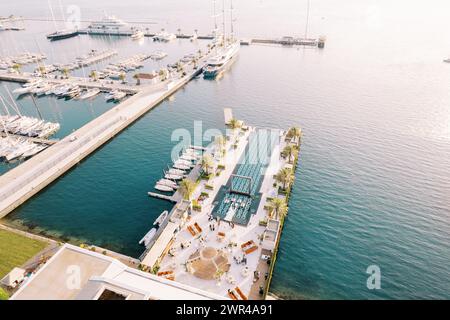 Partytische stehen auf einem langen Pier mit einem Swimmingpool und Yachten, die an der Seite verankert sind. Drohne Stockfoto