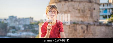 BANNER, LANGFORMAT-Junge, der türkisches Eis auf dem Hintergrund des Hidirlik-Turms in Antalya vor dem Hintergrund der mediterranen Bucht von isst Stockfoto