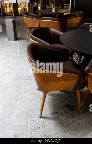 Braune Stühle mit Eichenmessern stehen um schwarze Tische in einem offenen Straßenbereich Stockfoto