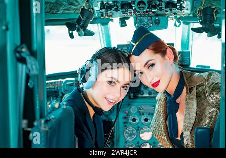 Zwei Frauen Piloten sitzen in der Kabine eines modernen Flugzeugs. Lächelnde Stewardess im Flugzeug. Porträt einer attraktiven Pilotenschülerin mit Headset Stockfoto