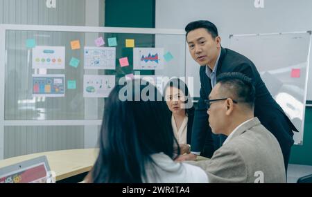 Eine Gruppe von Personen versammelt sich um einen Tisch mit einem Whiteboard hinter sich. Sie diskutieren etwas Wichtiges, und es gibt mehrere Poster Stockfoto