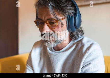 Ein Mann auf einem Sofa, der Kopfhörer trägt und Musik hört Stockfoto