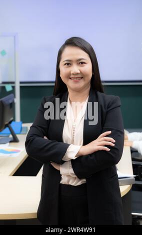 Eine Frau in schwarzem Anzug und weißem Hemd lächelt und steht mit überkreuzten Armen. Sie ist selbstbewusst und professionell Stockfoto