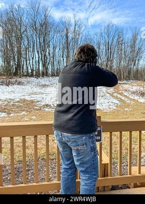 Ein junger Mann, der mit einer Schrotflinte auf einem Schießstand auf Tonträger schießt Stockfoto