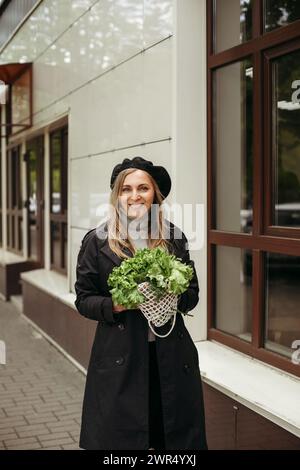 Eine Frau, die steht und einen Haufen Salat vor ihrem Gesicht hält. Vertikales Bild. Stockfoto