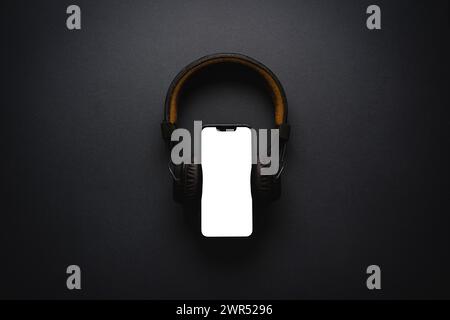 Schnurlose Over-Ear-Kopfhörer und Smartphone im Retro-Stil mit leerem Bildschirm auf dunkelgrauem Hintergrund Stockfoto