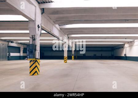 Innenraum eines großen leeren Lagerhauses. Industriegebäude. Mehrere Betonsäulen mit einem gestreiften schwarz-gelben Warnschild Stockfoto