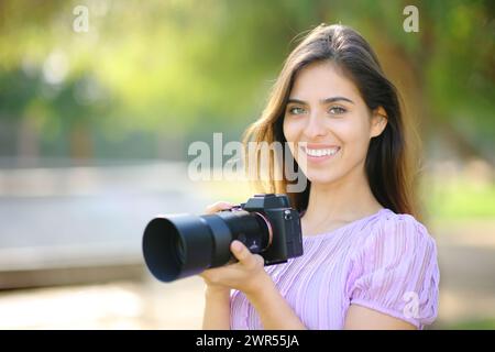 Glücklicher Fotograf posiert in der Kamera und hält spiegellos in einem Park Stockfoto